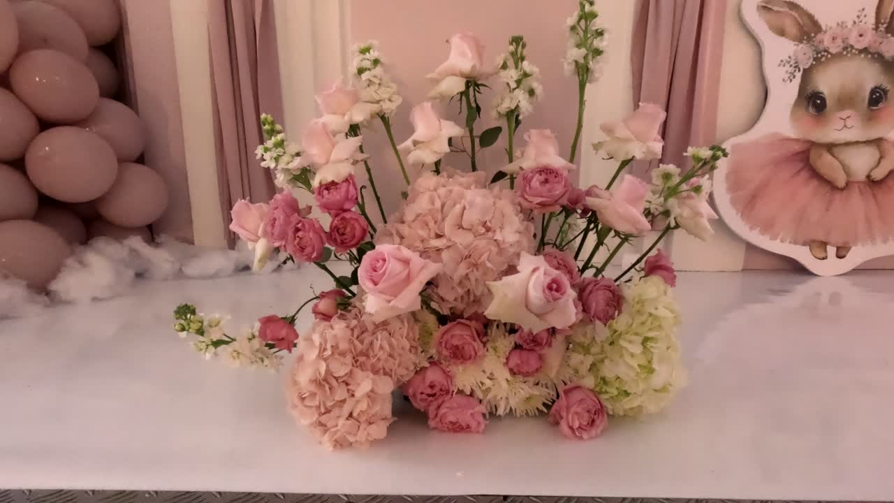 A floral display featuring pink roses, white blooms, and green accents is set up next to a bunny decoration. The scene is bright and cheerful for a children's celebration