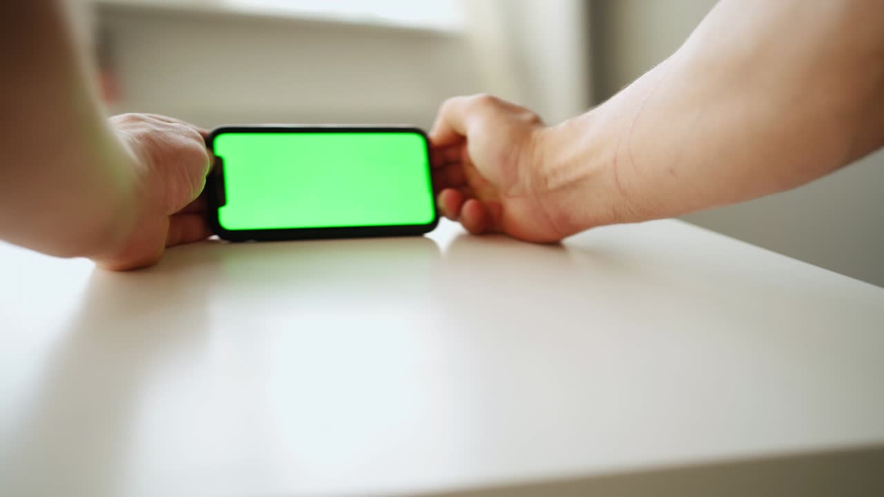클로즈업, 한 남자가 테이블에 서 있는 동안 녹색 화면으로 스마트폰을 사용합니다.
