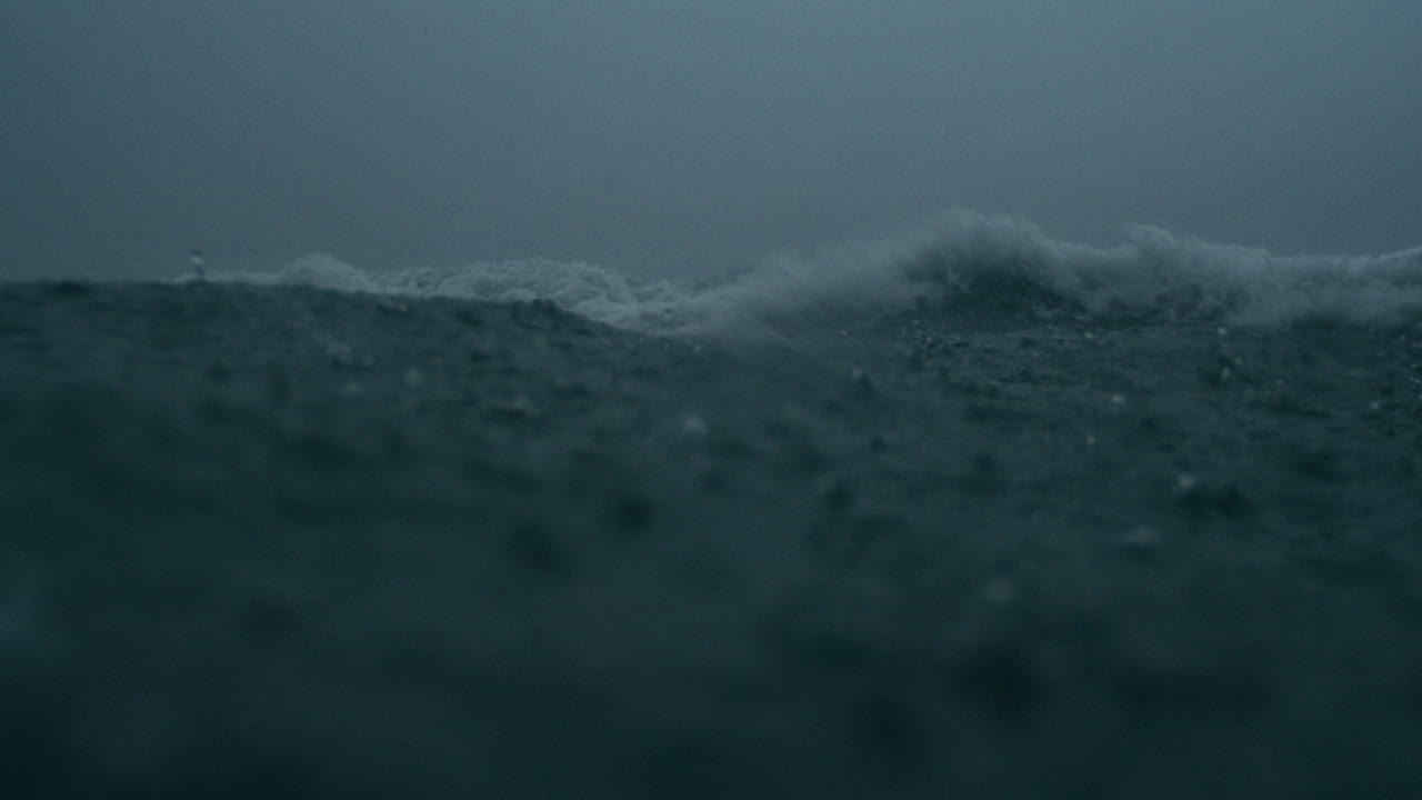 Slow falling raindrops break across turbulent waters beneath stormy clouds