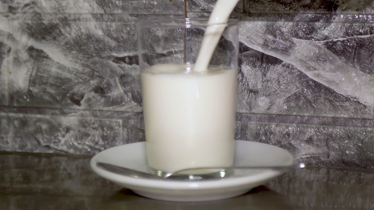 llenando un vaso de leche entera de cartón en un pequeño plato blanco con cuchara de plata