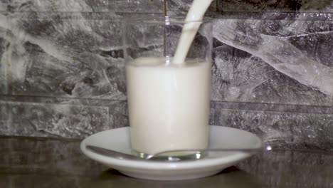 filling a glass of whole milk from carton on small white plate with silver spoon