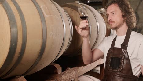 authentic shot of successful male sommelier is tasting a flavor and checking white wine quality poured in transparent glass in a wine cellar.