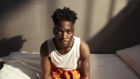 portrait of young black prisoner sitting on bed in jail