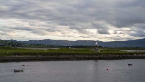 lapso de tiempo del puerto del faro con barcos estacionados en primer plano y nubes que se mueven rápidamente en el cielo en irlanda