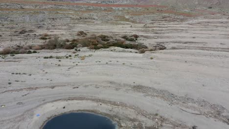 Luftflug-über-Einen-Wasserteich-Am-Toten-Meer-Und-Hinauf-über-Die-Mit-Roten-Blumen-Bedeckten-Hügel-Der-Wüstenküste,-Drohnenweitschuss,-Israel