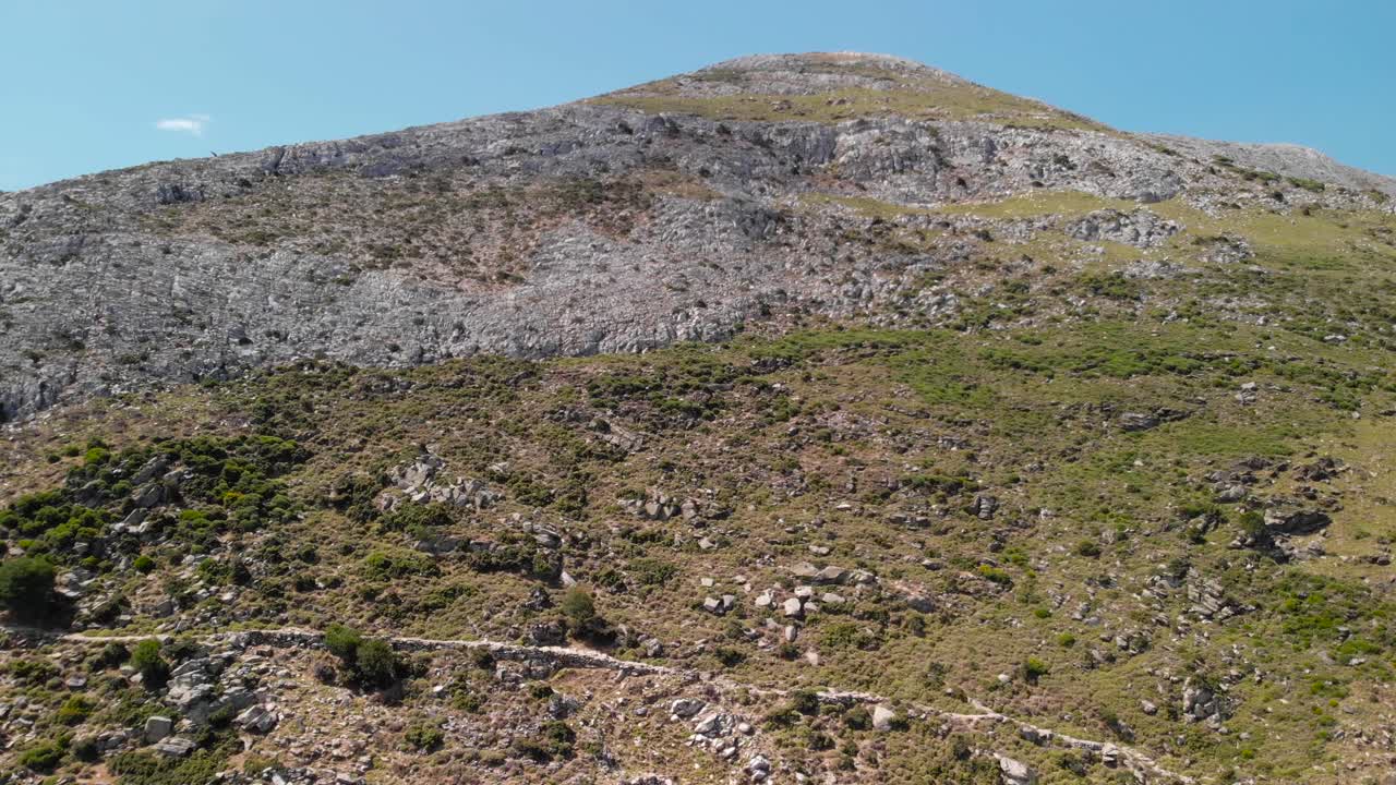 antena de ascenso lento sobre una montaña rocosa y árida con camino y cielo azul