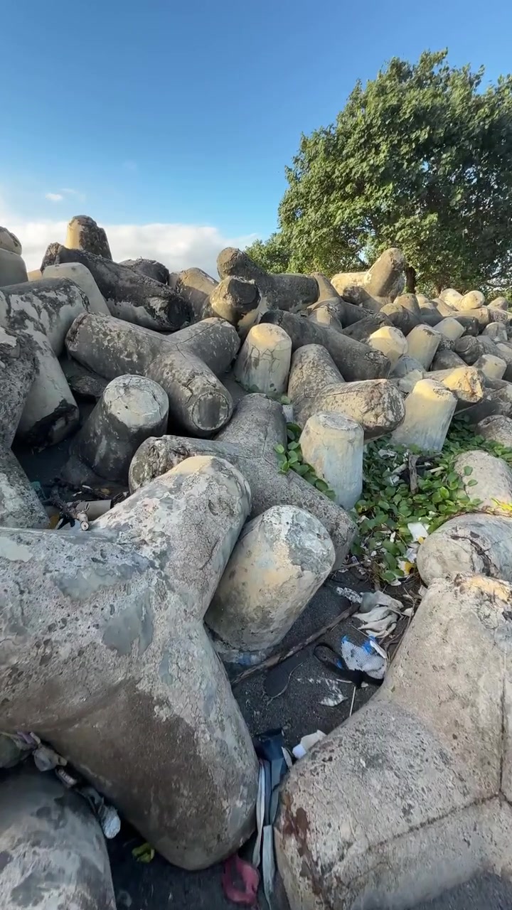 Pila di tetrapodi frangiflutti in cemento su una spiaggia inquinata.