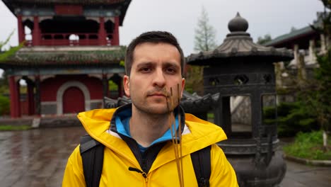 un turista sostiene palos de incienso mirando a la cámara en el patio del templo de tiananmen, china