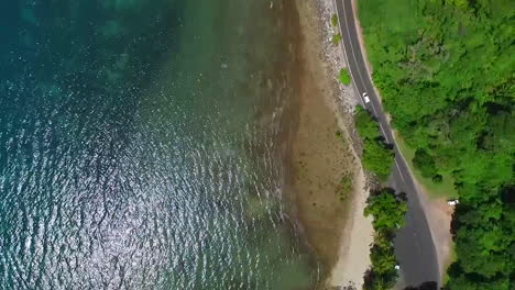 birdseye view following a white car along a stretch of coastal road on a sunny day