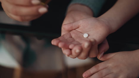 woman puts small medicine on little daughter palm in room