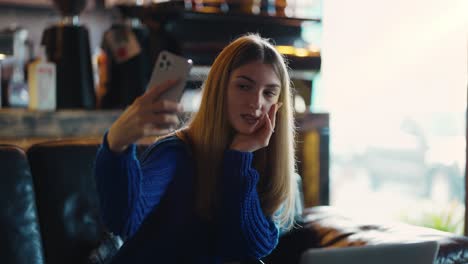 Attraktive-Frau-Schaut-Auf-Ihr-Handy-Und-Macht-Ein-Selfie-In-Einem-Modernen-Café