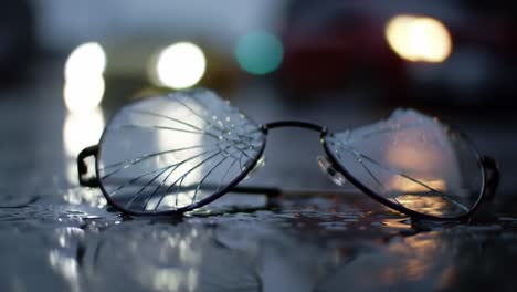in the darkness of night, shattered glasses lie on a waterlogged street, reflecting distant lights. the scene evokes a sense of a recent accident, with rain highlighting the chaos.