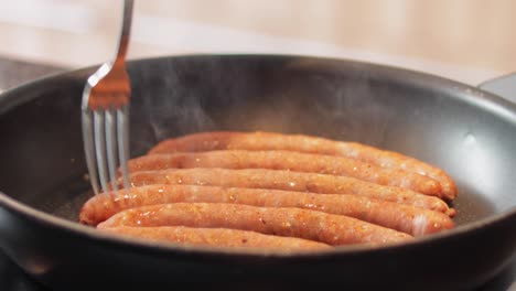 thin brown pork sausages cooking in frying pan on electric stove top indoors, close-up still shot