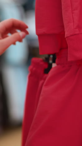 close-up shot of a hand in a brown jacket reaching for a red garment in a clothing store. the texture and detail of the red fabric, as well as the casual action of browsing through clothing racks
