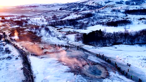 vista panorámica con un dron de un geyser en geysir, islandia. el humo está saliendo del geyser con la gente caminando alrededor del geyser, bajo la puesta de sol roja.