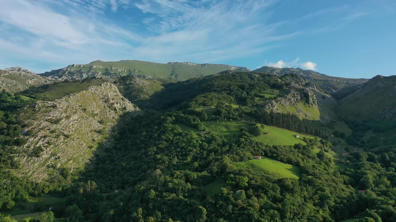 Volo laterale con un drone in montagne calcaree, tra foreste di querce e faggi, che mostra pendii ripidi, stalle, prati verdi e cime a plateau in una giornata estiva in Cantabria, Spagna.