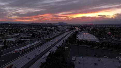 Unglaublich-Dynamischer-Sonnenuntergang-Mit-Wechselnden-Orange--Und-Rosafarbenen-Wolken-über-Dem-California-Highway-10-Mit-Geschäftigem-Verkehr,-Der-Bei-Sonnenuntergang-Immer-Dunkler-Wird.-Luftbild-Dolly-Push