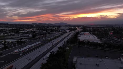incredible dynamic sunset with changing clouds orange and pink over california highway 10 with busy traffic scene getting darker as the sun sets aerial dolly push