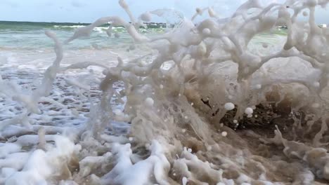 the sea wave crashing into a small rock on a sandy beach slow motion clip