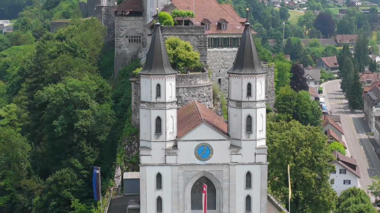 Close-up aerial of the church towers with forested hillside and town background