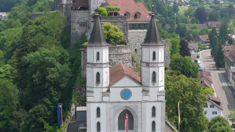 close-up aerial of the church towers with forested hillside and town background