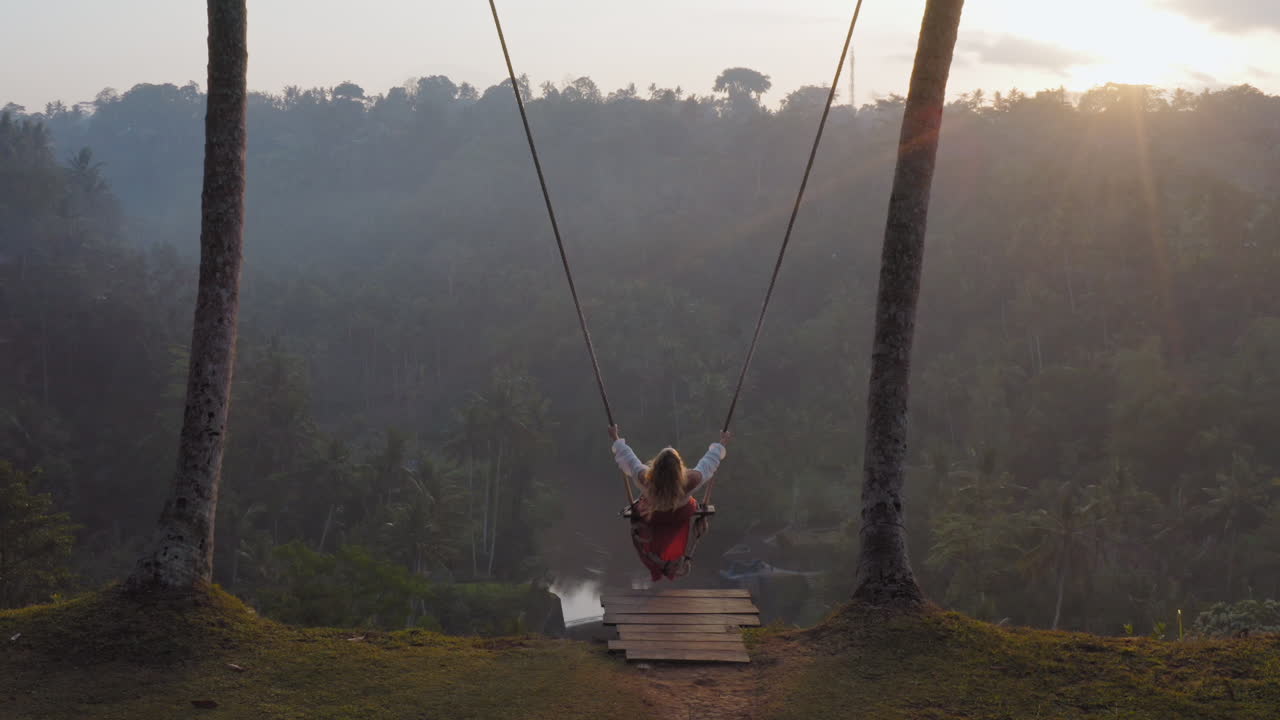 vista aerea donna che oscilla sopra la foresta pluviale tropicale all'alba seduta sull'altalena con vista sul fiume che si diverte in vacanza libertà di viaggio