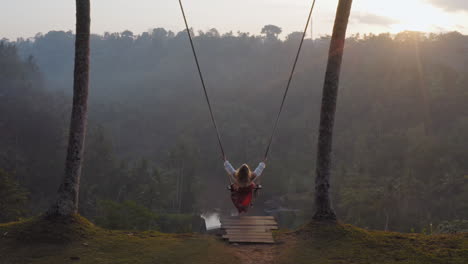 aerial view woman swinging over tropical rainforest at sunrise sitting on swing with view of river enjoying having fun on holiday travel freedom