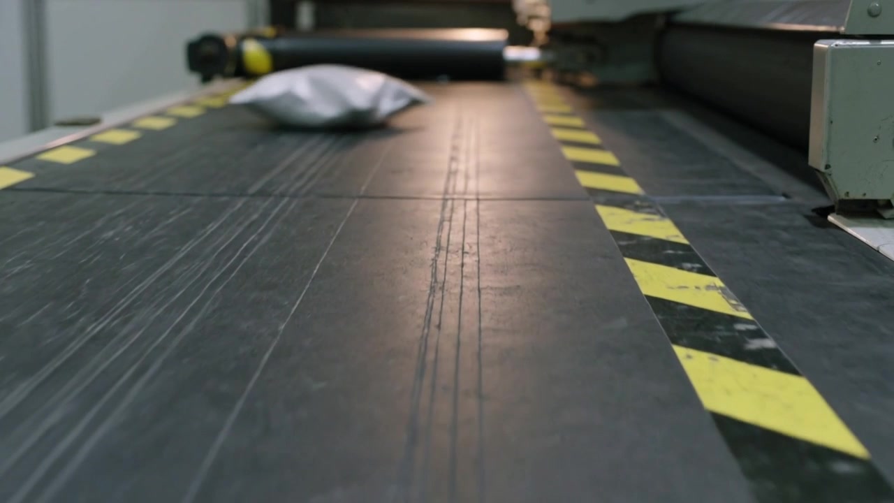 Nastro trasportatore con nastro di pericolo in movimento che sposta pacchi in un impianto, con un pacco che attiva un deviatore per lo smistamento.