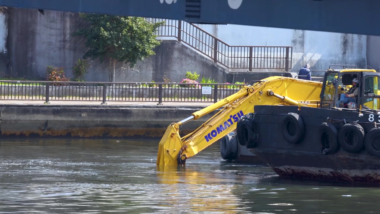 Escavatore industriale su una chiatta esegue operazioni di dragaggio in un canale fluviale di Tokyo, Giappone