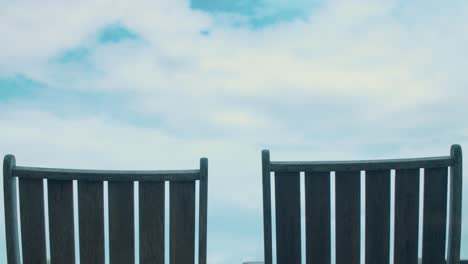 Timelapse-of-large,-fluffy-white-clouds-floating-across-the-sky-as-two-wooden,-beach-chairs-sit-and-gawk-at-the-serenity