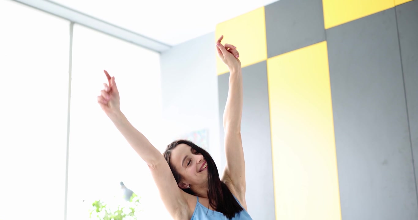 暖かい朝の光が差し込む、明るく心地よい寝室で元気にストレッチをする若い女性