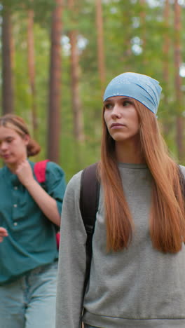 excursionistas caminando por el sendero del bosque, mujer en bandana azul y sudadera gris mira a su alrededor pensativo, mientras que el compañero en camisa verde ajusta el cuello