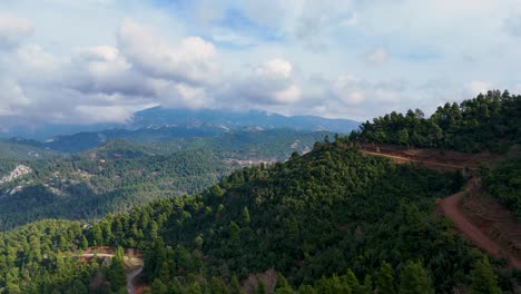 Vista-Aérea-Sobre-Un-Bosque-Verde-Con-Altos-Picos-Montañosos-Y-Un-Motociclista-En-La-Carretera-De-Abajo,-Isla-De-Evia,-Grecia