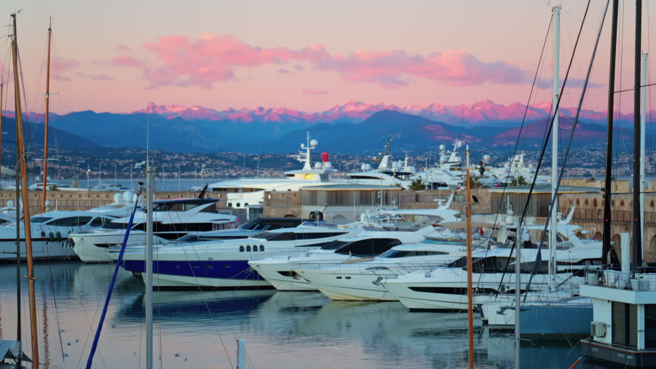Juan-les-Pins, France - January 25, 2025: Multiple white boats docked in the harbour in Antibes with the mountains on the background at sunset