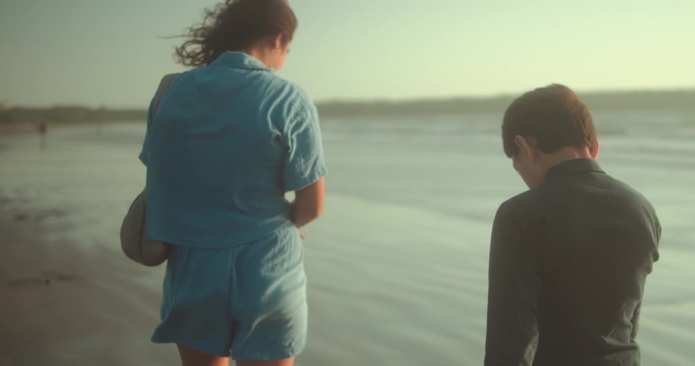 Una donna e un bambino che camminano insieme lungo una spiaggia sabbiosa al tramonto. Un caldo momento di vacanza in famiglia vicino all'oceano con un'atmosfera costiera pacifica
