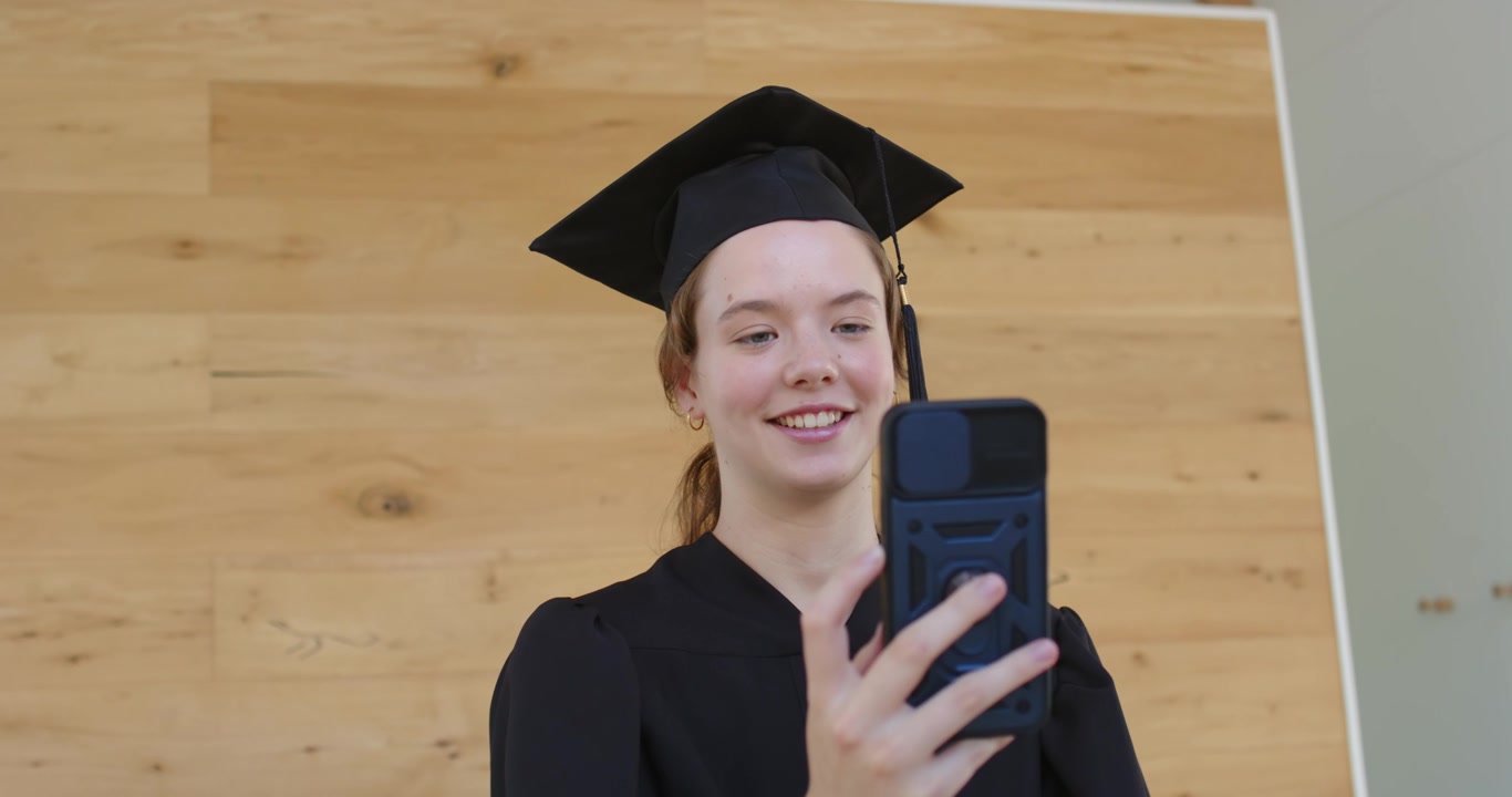 Laureata sorridente, con toga e tocco, che tiene in mano uno smartphone e registra un messaggio dopo la cerimonia.