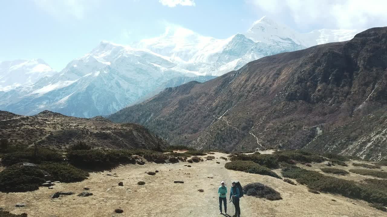 una pareja de senderismo en el valle de manang, annapurna circus trek, himalaya, nepal, con vistas a la cadena de annapurna y gangapurna. paisaje seco y desolado. altos picos de montaña, cubiertos de nieve.