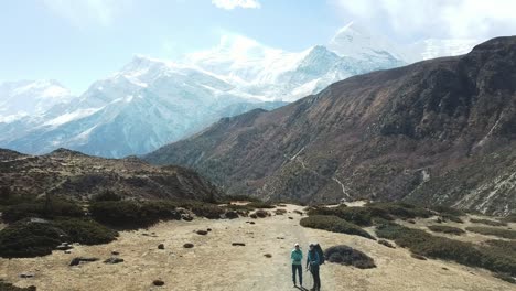 a couple trekking in the manang valley, annapurna circus trek, himalayas, nepal, with the view on annapurna chain and gangapurna. dry and desolated landscape.  high mountain peaks, covered with snow.