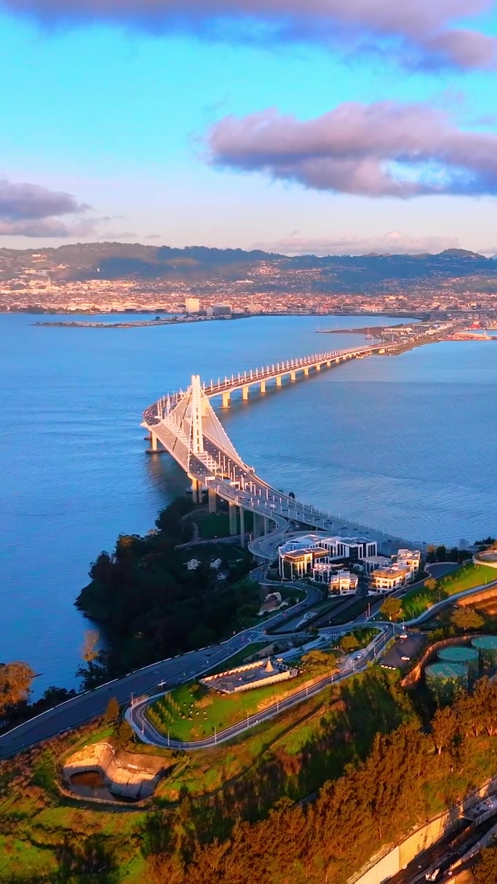 Vista elevada da nova extensão da Bay Bridge perto de Yerba Buena Island. Imagem de drone do design de suspensão autoancorada, colinas verdes e acesso à rodovia ao pôr do sol. Vídeo vertical