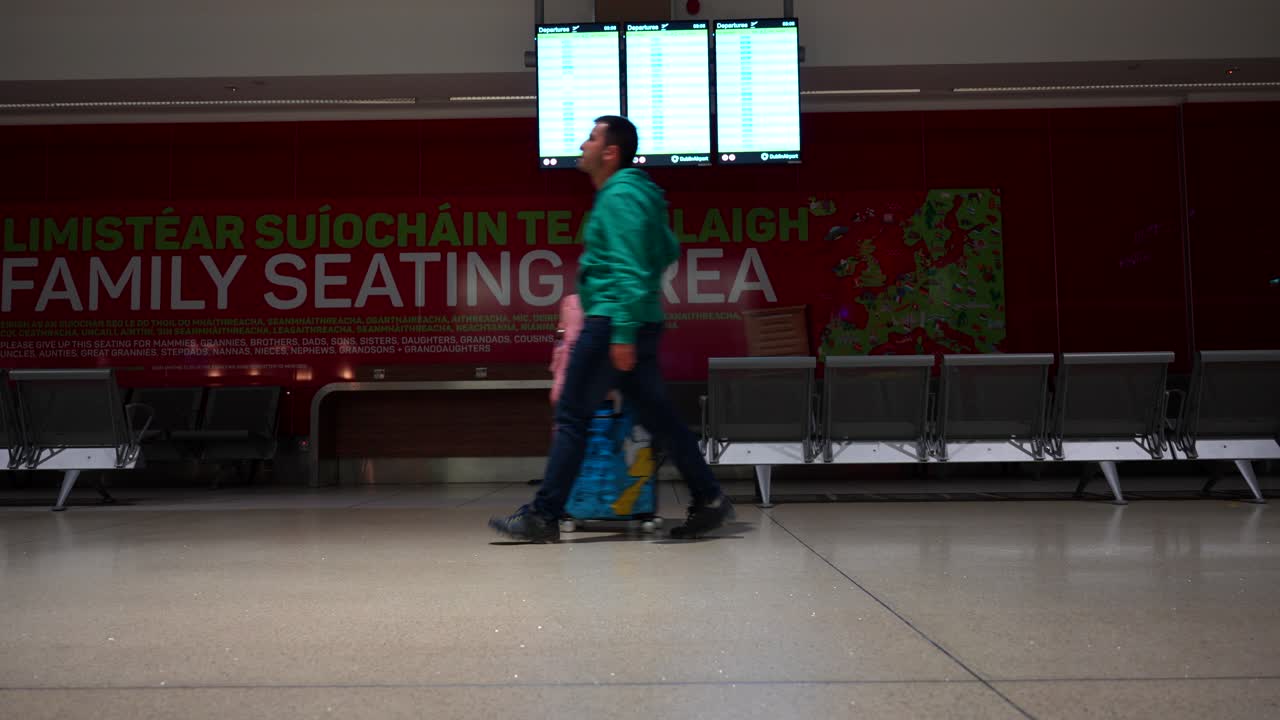 hombre caminando con equipaje frente al tablero de información en el aeropuerto de dublín