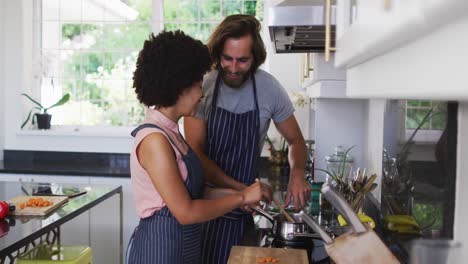 pareja de raza mixta usando delantales cocinando comida juntos en la cocina en casa