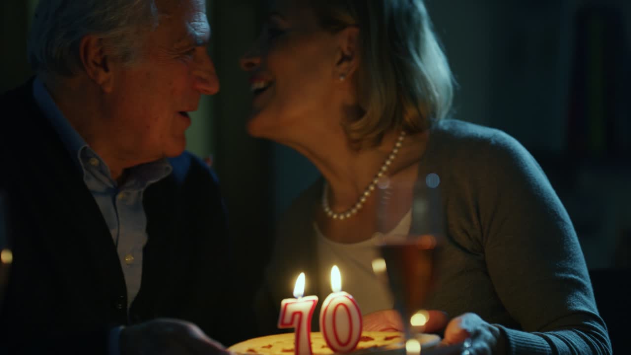 한 고령 여성이 집에서 생일을 축하하기 위해 케이크의 불을 불고 있습니다.