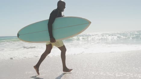 Lächelndes-älteres-Afroamerikanisches-Paar,-Das-Mit-Surfbrettern-Am-Sonnigen-Strand-Läuft