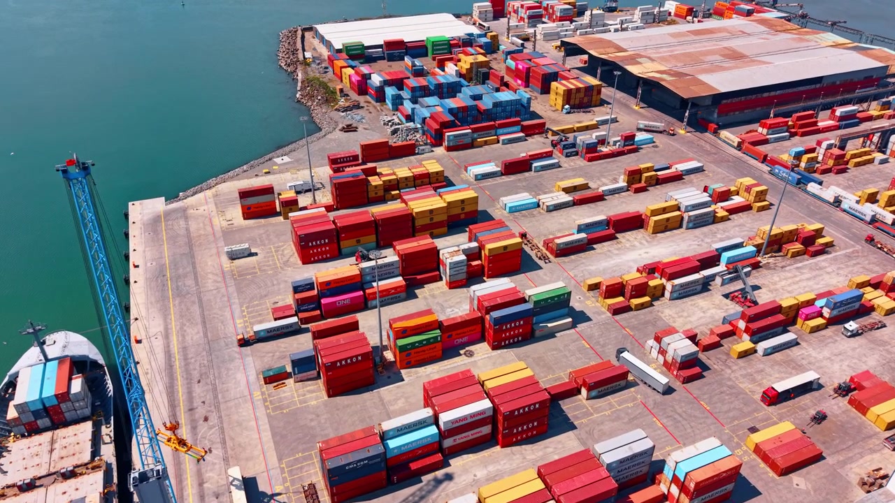 Burgas, Bulgaria, 1 May 2026: Container yard and cargo ship at seaport quay. High angle drone view of container stacks, quay crane, cargo ship, trucks and paved terminal markings.