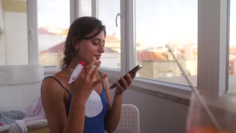 young woman talks on smartphone while holding a spray bottle on a balcony