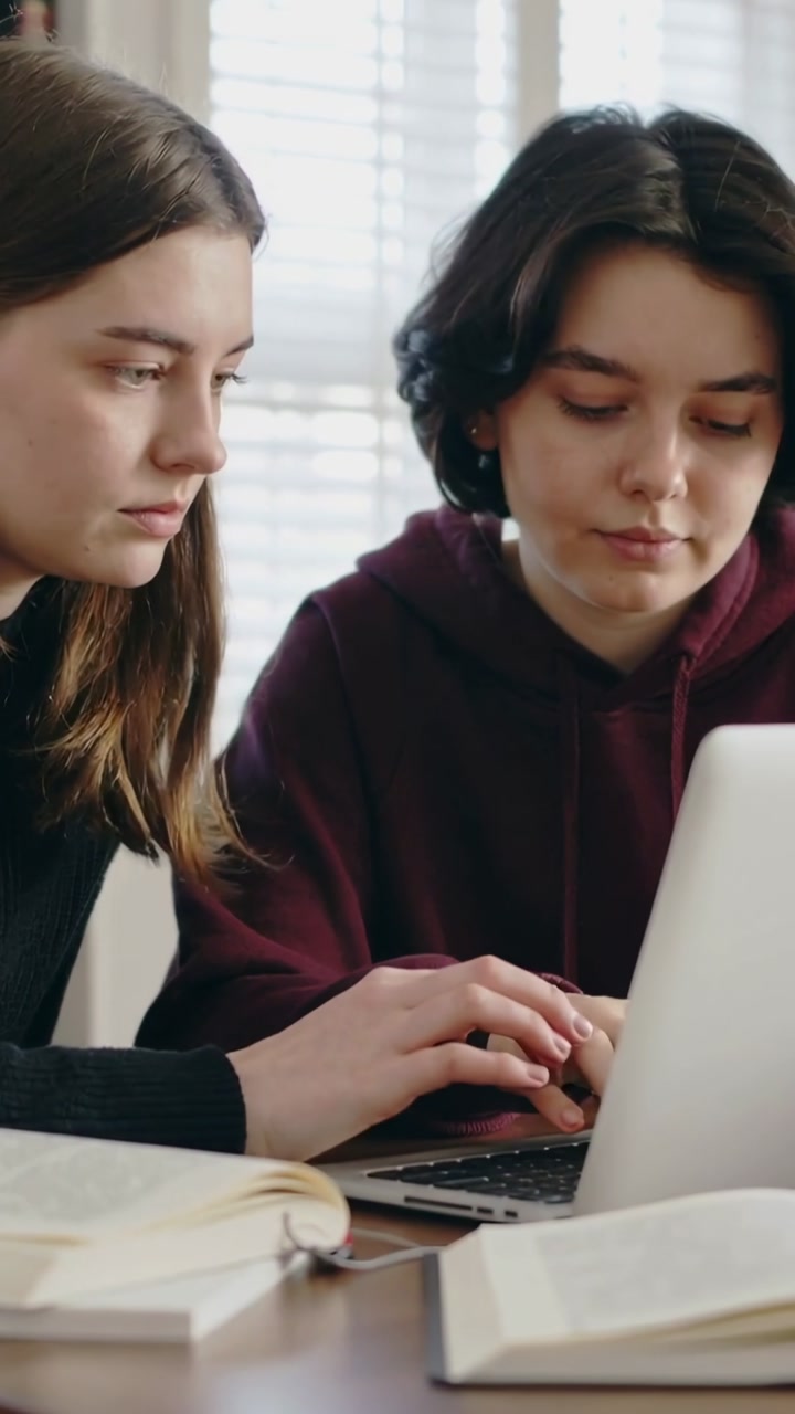 Vertical video: Placing hands on keyboard, right student typing on laptop at table, studying books