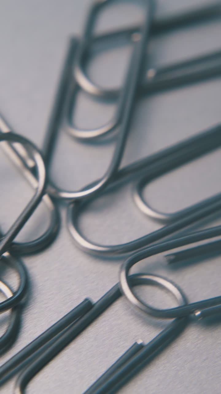 motion past small heap of shiny metal paperclips lying on clean grey surface extreme close view
