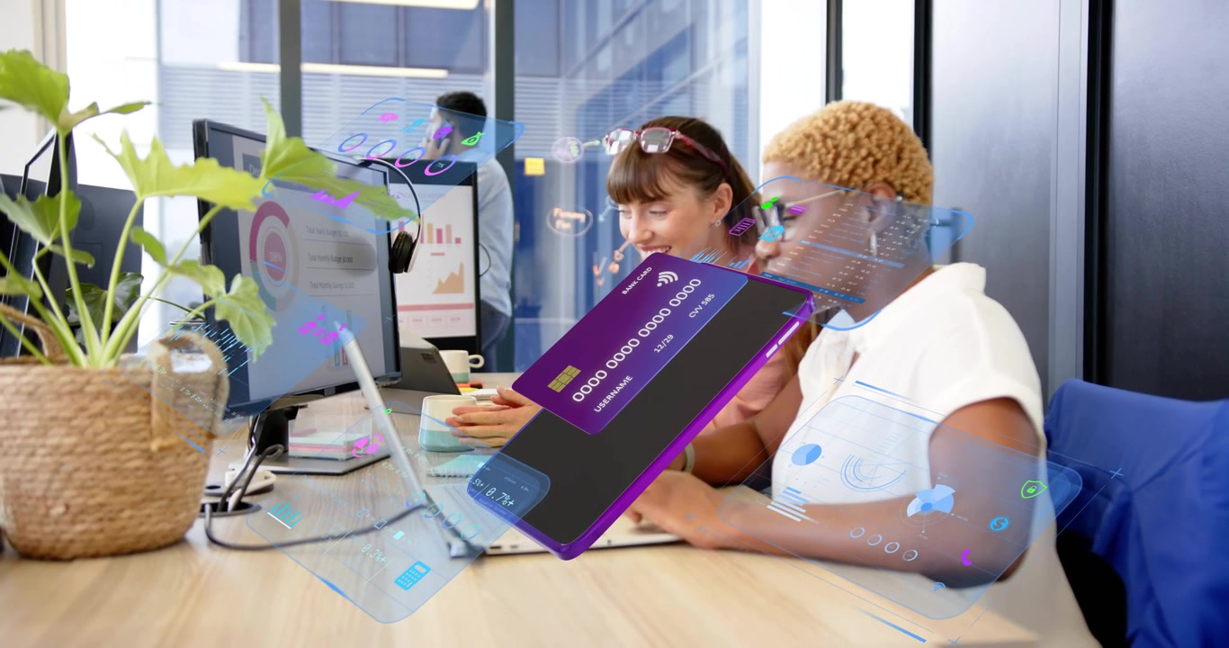 Two women pointing at laptop in business animating phone, credit card charts orbiting for analysis