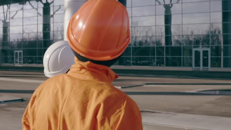 two workers in orange uniform and helmet pointing at the building and examining the object. slow motion