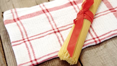 Bunch of raw spaghetti tied up with red ribbon on red and white napkin on wooden background